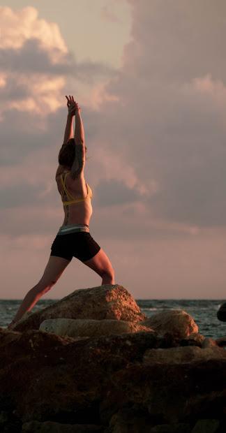 A yoga pose performed on rocks by the water at sunset